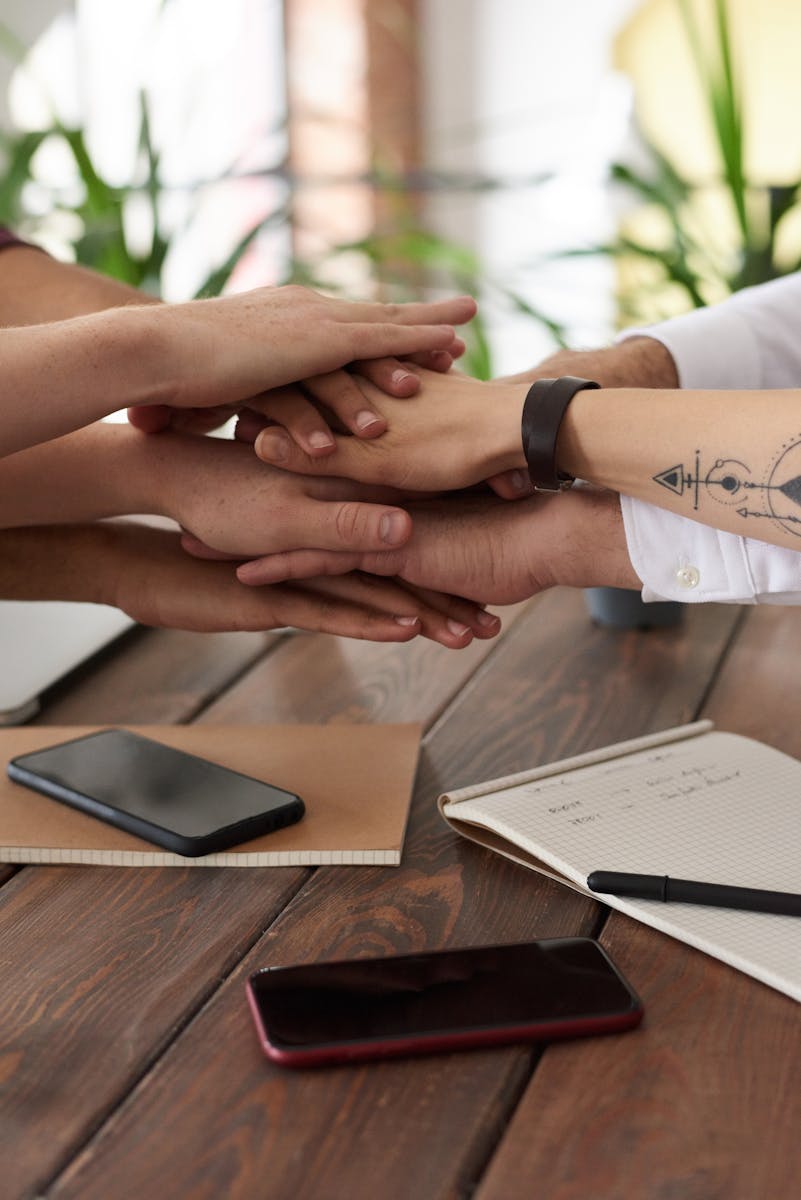Marketing en Amazon y Marketplaces 6 Hands from a diverse team stack on a table symbolizing unity and teamwork in a modern office setting.