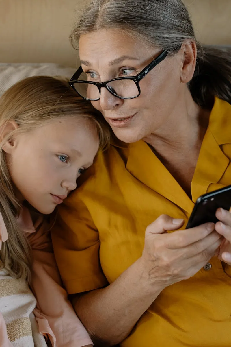 Social Media 3 Mujer mayor y niña disfrutando juntas, creando lazos a través de un smartphone en interiores.
