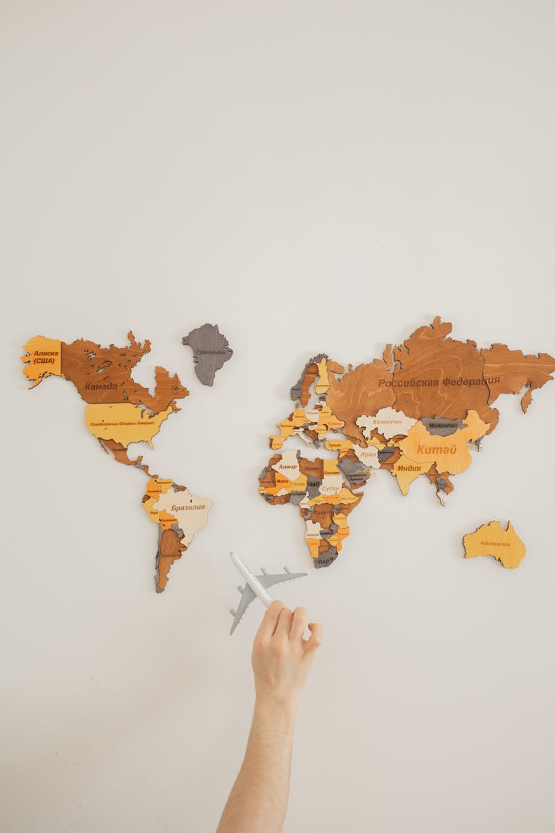 International Marketing & New Market Entry 1 A hand holding a toy plane points to a colorful decorative world map on a wall.