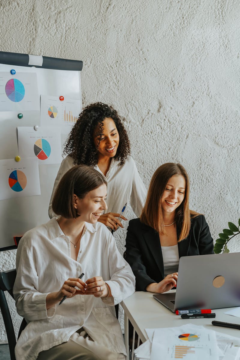 SEO 4 Three businesswomen collaborate with graphs and a laptop in a modern office setting.
