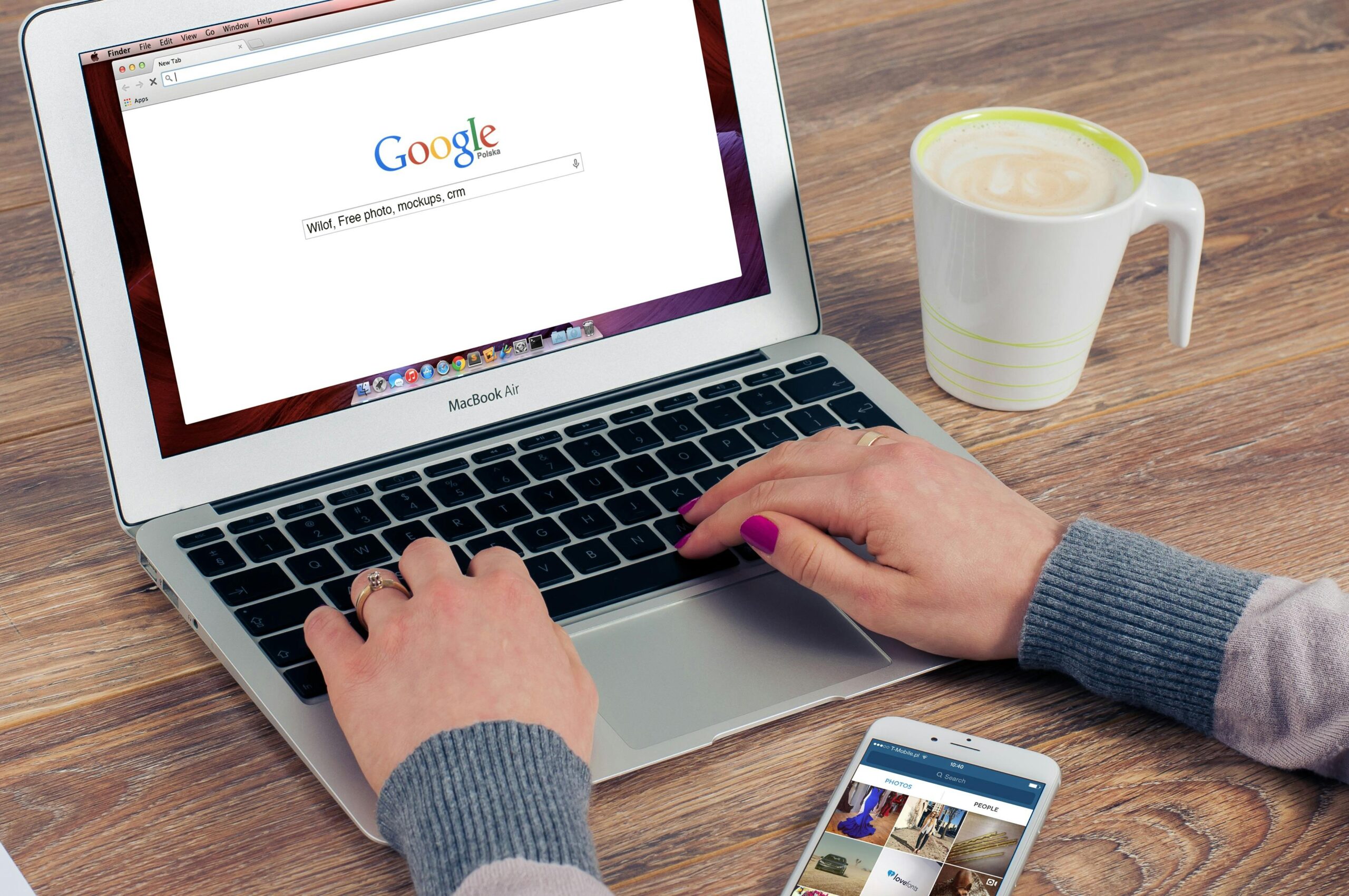 SEO 7 Hands typing on MacBook Air with Google search open, coffee nearby.
