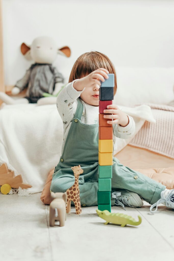 Espacios de Crianza y Centros Familiares 1 A cute child stacks colorful wooden blocks while playing indoors, surrounded by toys.