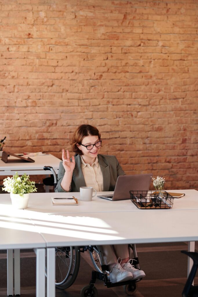 Doulas, Comadronas y Psicólogas Perinatales 1 A cheerful businesswoman in a wheelchair working remotely from a modern office setting.