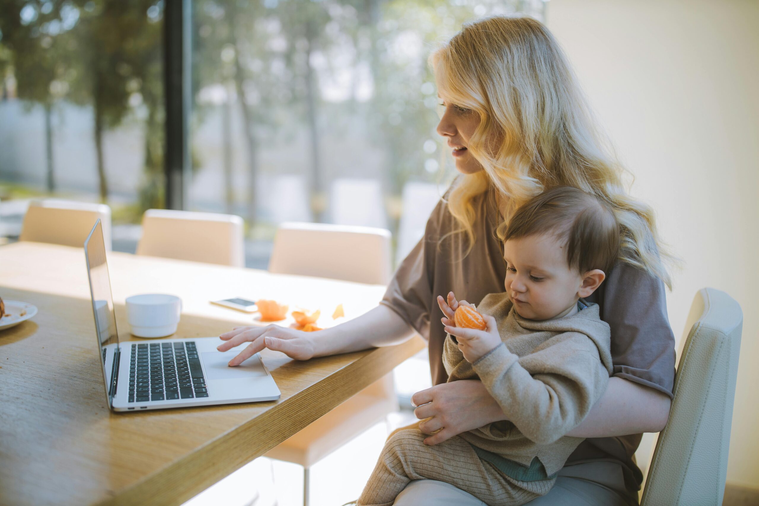 Who we help 12 A mother works on a laptop at home while holding her baby, showcasing remote working and parenting.