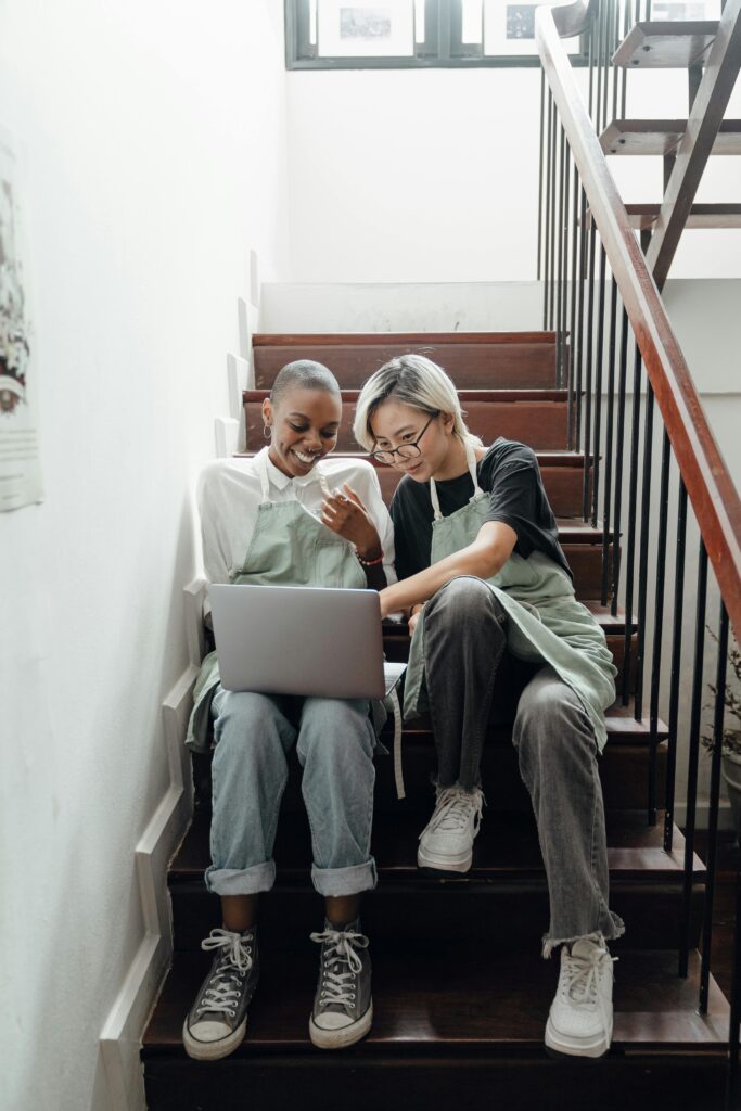Amazon & Marketplace Marketing 5 Full body of positive young diverse female friends in trendy clothes and aprons watching funny video on laptop sitting on staircase