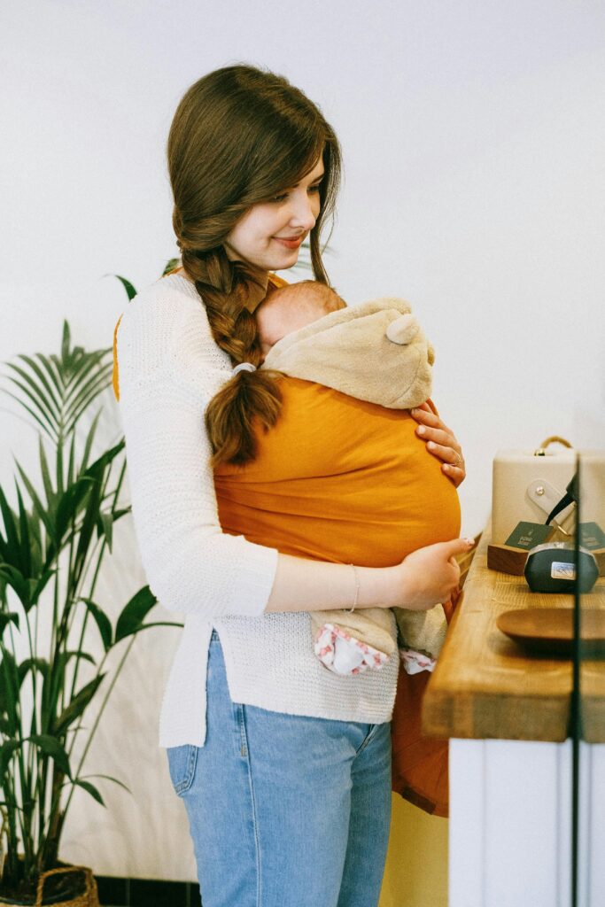 Social Media Marketing for Children's Brands 6 A warm moment of a mother holding her baby in a sling inside a cozy cafe.