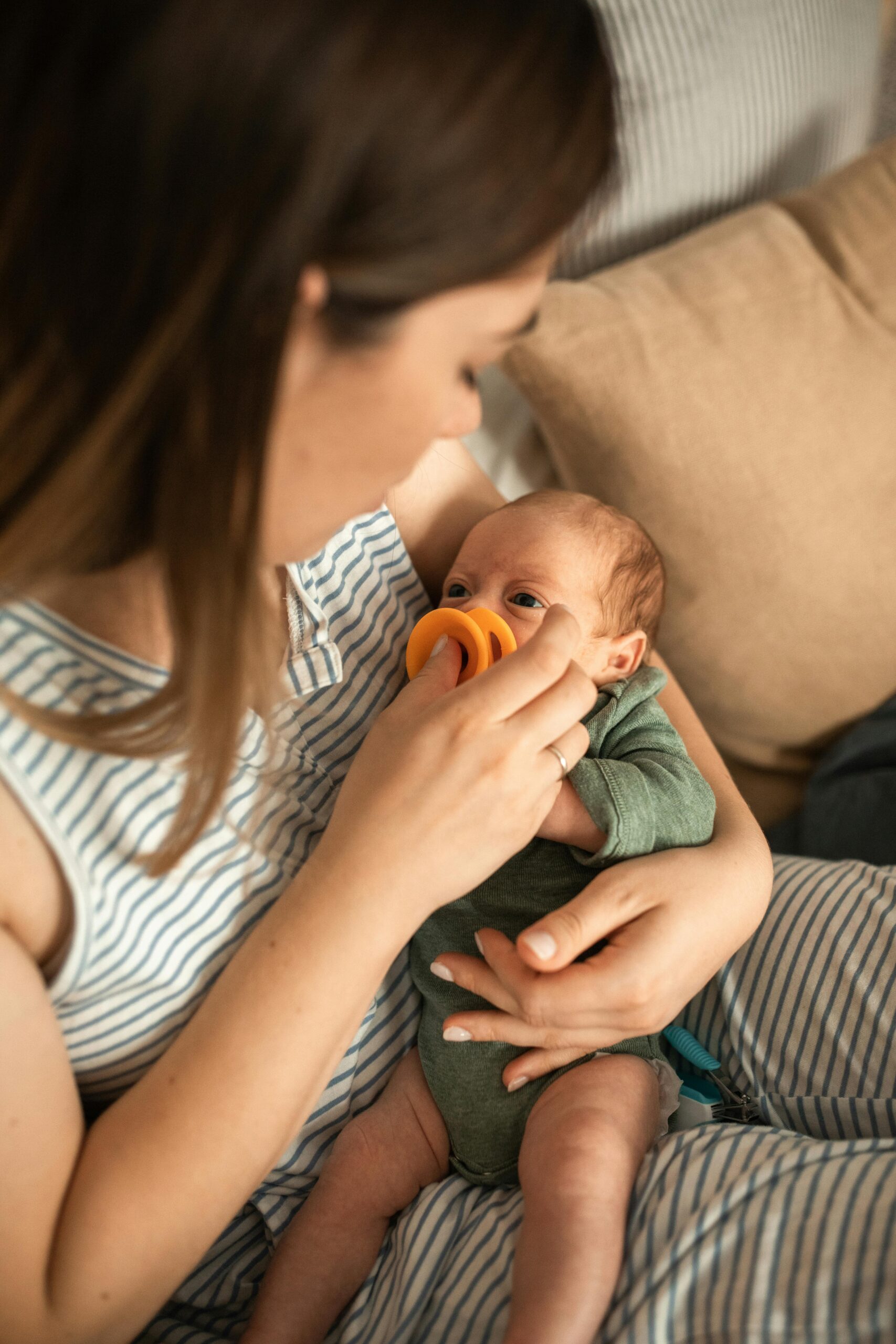 Feeding & Nutrition Products 1 A mother tenderly feeds her newborn baby with a bright orange pacifier indoors.