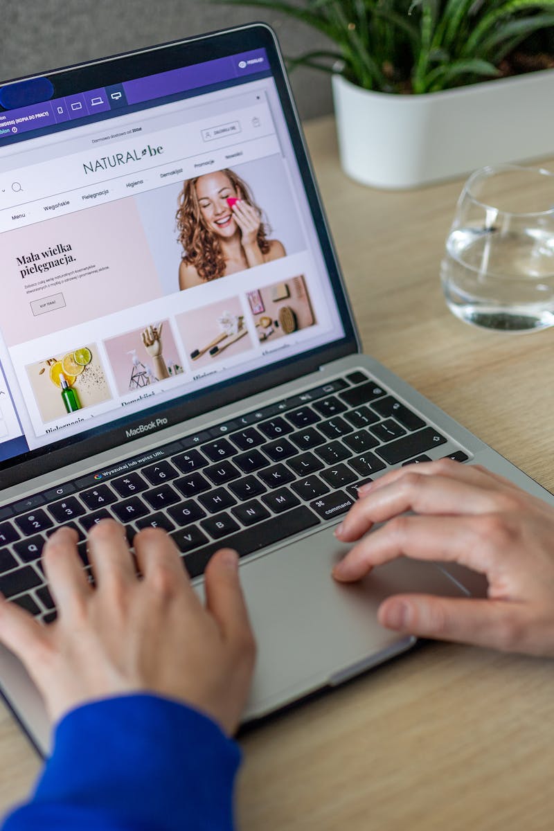 Hands typing on a laptop showing an e-commerce website in a modern office setting.