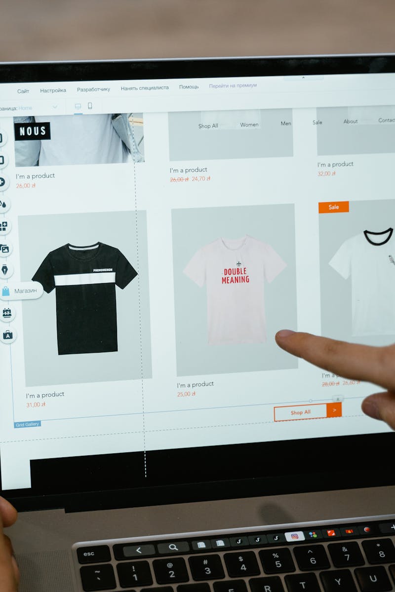 A person points to t-shirt options in an online store on a laptop screen.