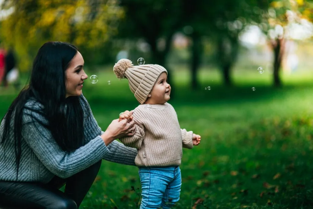A joyful moment with mother and child playing with bubbles outdoors in a park.