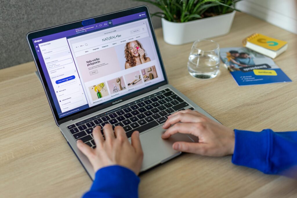 Manos escribiendo en un portátil que muestra un sitio web de comercio electrónico en un entorno de oficina moderno.