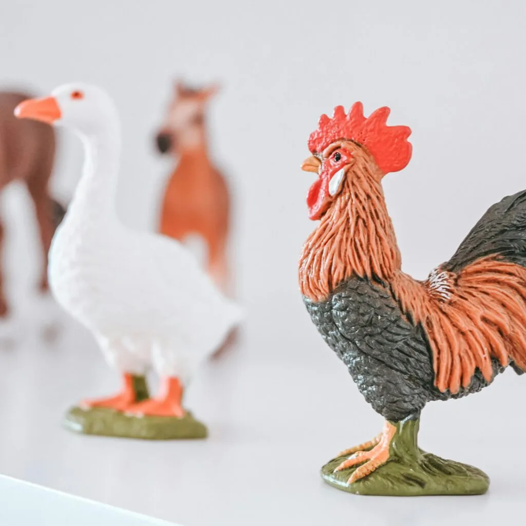 Close-up of colorful rooster and goose toy models with farm background.