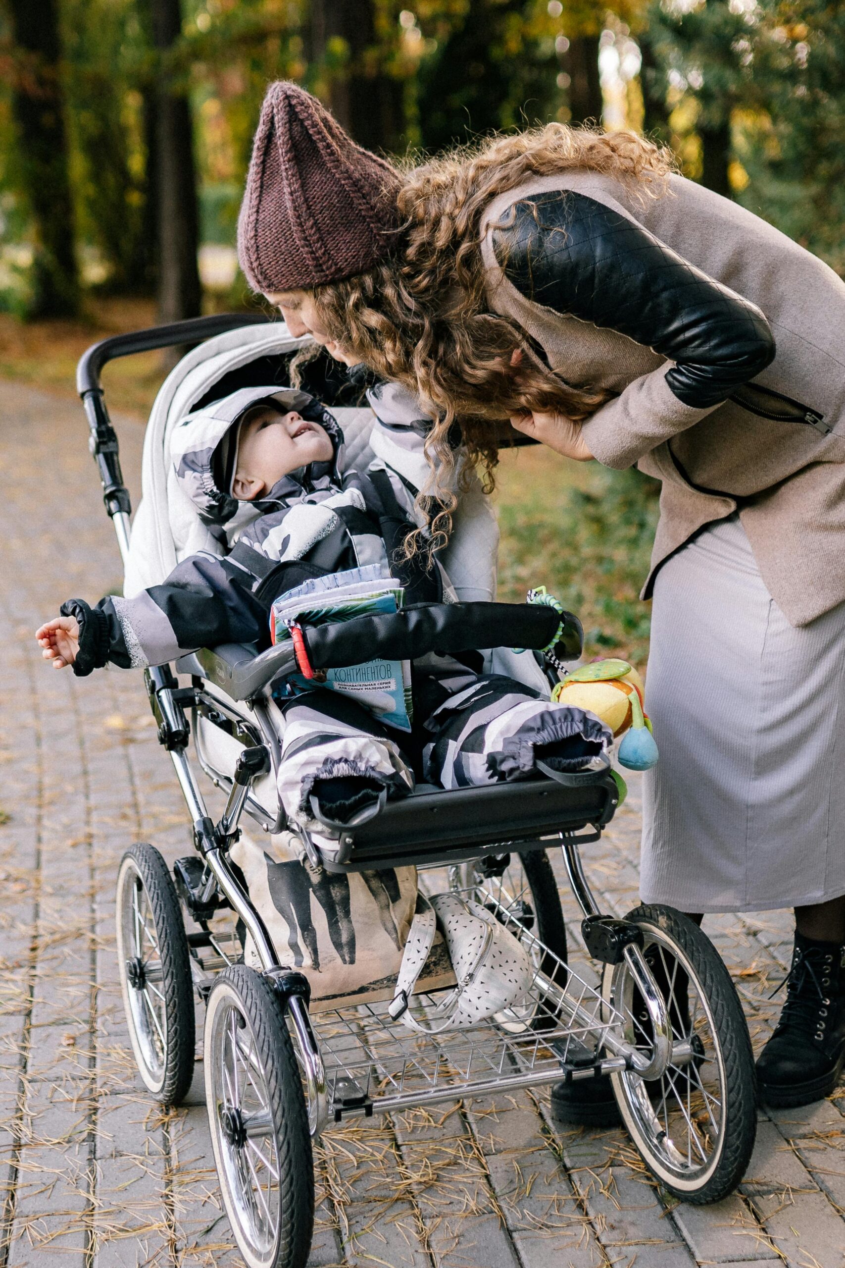 A mother bends over a stroller in a park during autumn, enjoying quality time with her baby.