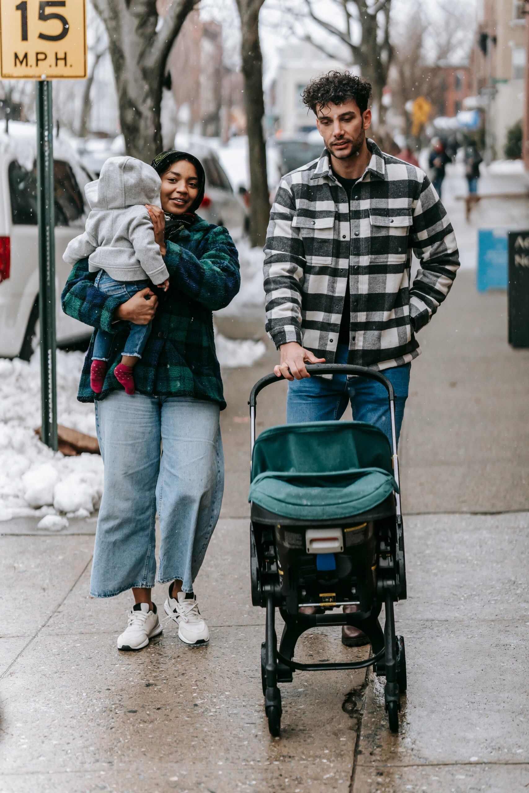 Full length of happy young diverse family with baby in warm stylish clothes walking on city street on winter day