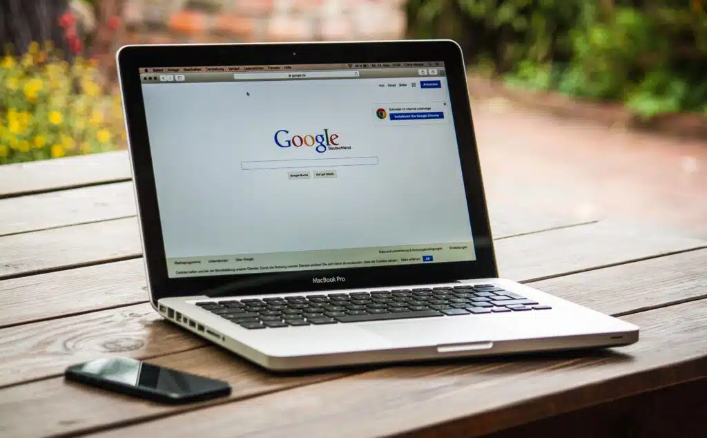 Qué páginas necesita una marca infantil para posicionar en Google 3 A MacBook Pro displaying Google Search on a wooden table outdoors, next to a smartphone.