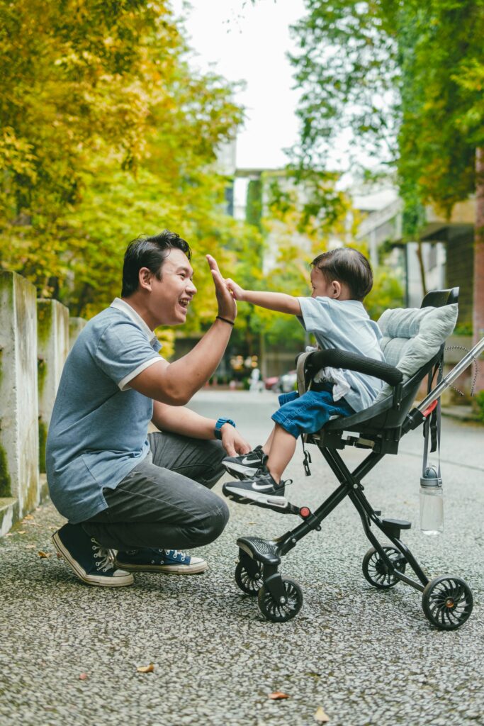 Father and young child sharing a high five on a city street, surrounded by greenery.