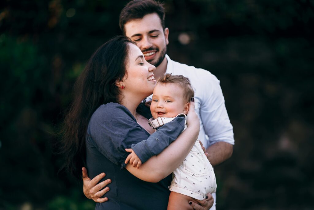A cheerful family enjoys a loving moment outdoors, embracing their baby.