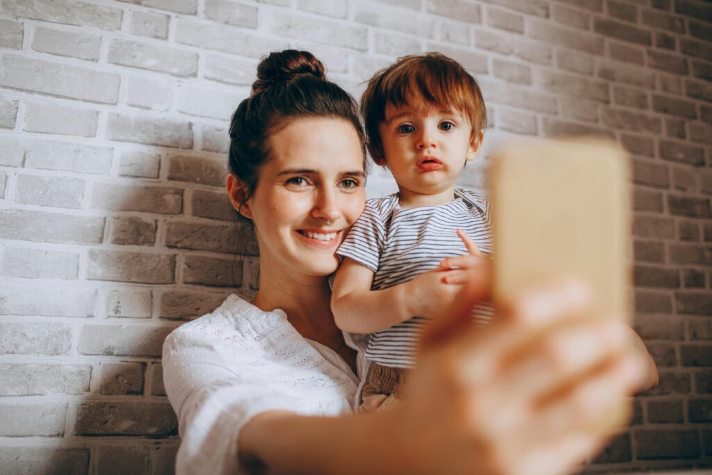 A happy mother taking a selfie with her young son against a brick wall backdrop.