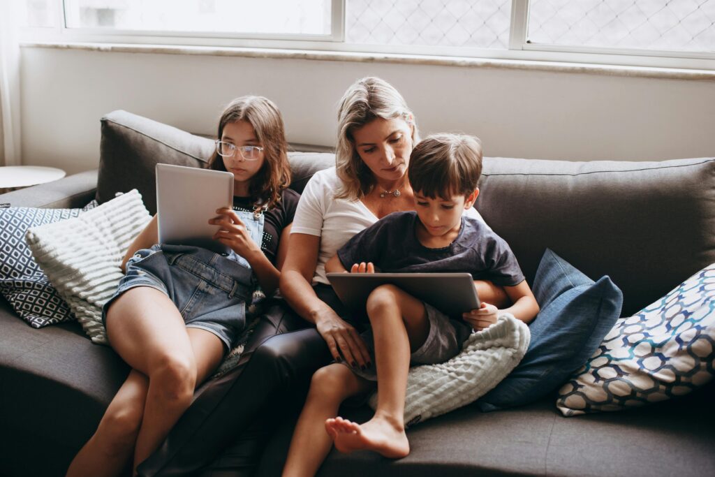 A family enjoying leisure time indoors, using tablets together on a sofa.
