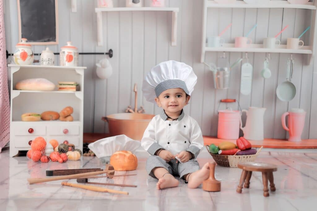 Cute child dressed as a chef in a toy kitchen with utensils and play food.