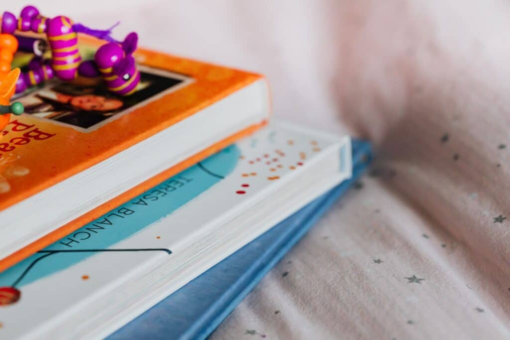 Close-up of colorful children's books stacked with a playful toy on top indoors.