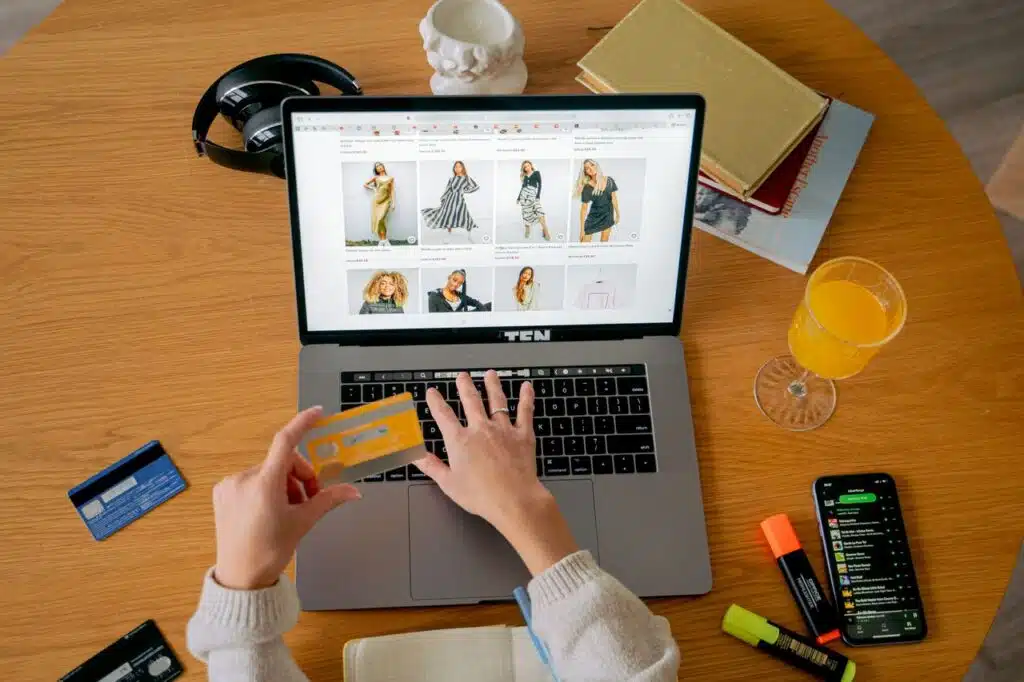 Configurar tallas y variantes en Shopify para moda infantil 11 Hands holding credit card making online purchase on laptop at wooden desk with various items.