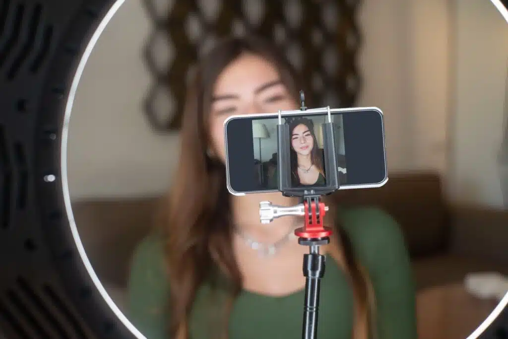 Briefing para influencers de maternidad: cómo alinear marca, creadora y confianza 15 A young woman live streams from home using a smartphone and ring light setup.