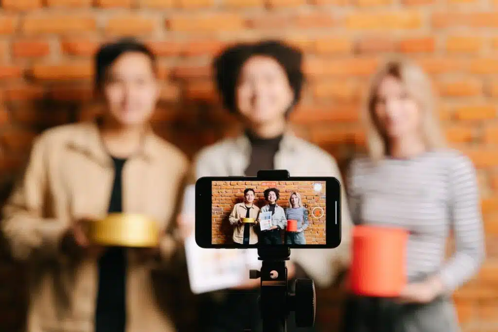 Métricas para campañas de influencer marketing de maternidad 10 A diverse team of vloggers recording a video with a smartphone against a brick wall backdrop.