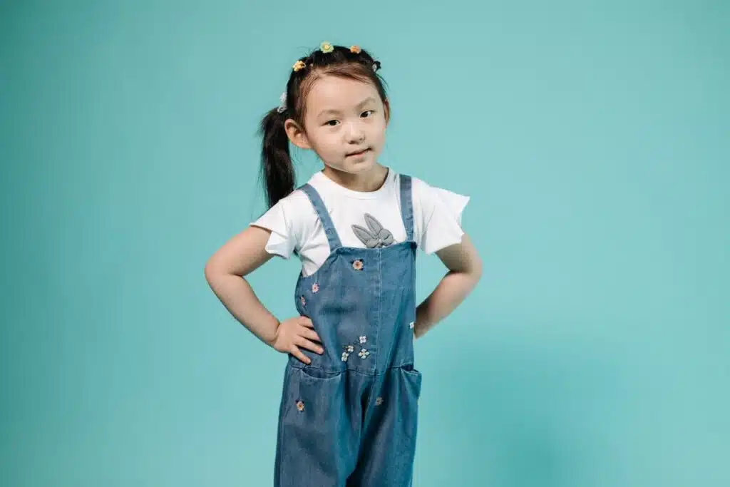 Publicidad responsable con menores: claves para marcas infantiles 14 Adorable young girl with hands on her hips posing in a denim overall on a blue background.