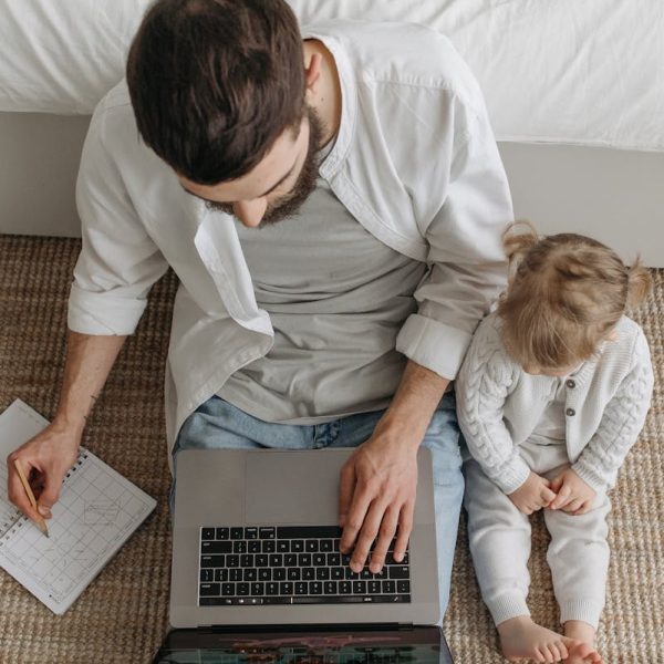 Father working on laptop with daughter by his side, a cozy home setting.