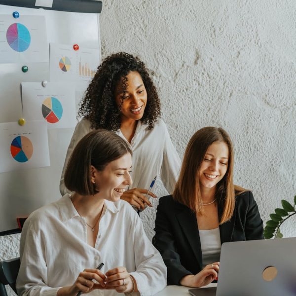 Three businesswomen collaborate with graphs and a laptop in a modern office setting.