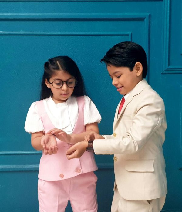 Two children in formal clothing standing together with a blue backdrop.