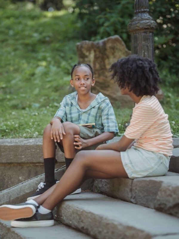 Two teenagers sitting on stone steps, enjoying a casual outdoor conversation in a park setting.