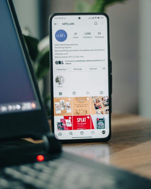 Vertical shot of a smartphone displaying an Instagram profile next to a laptop, representing social media engagement.