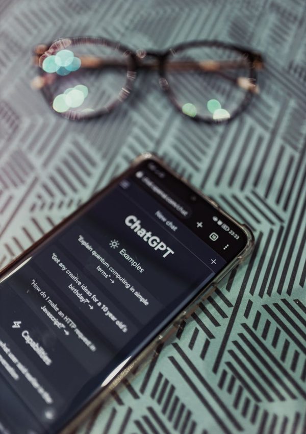 Smartphone with ChatGPT app interface next to eyeglasses on patterned surface.