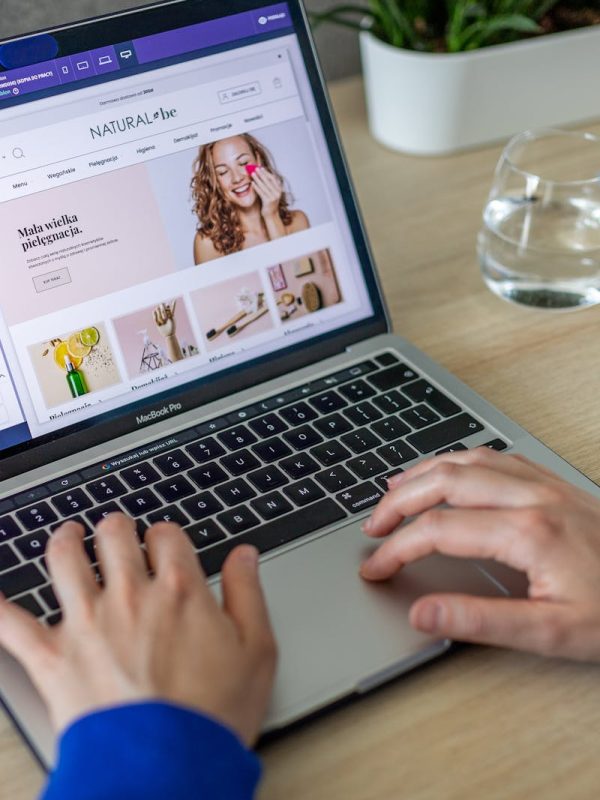 Hands typing on a laptop showing an e-commerce website in a modern office setting.