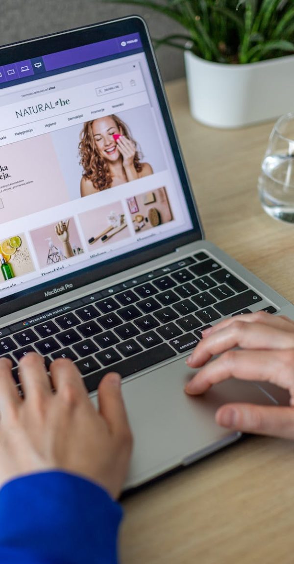 Hands typing on a laptop showing an e-commerce website in a modern office setting.