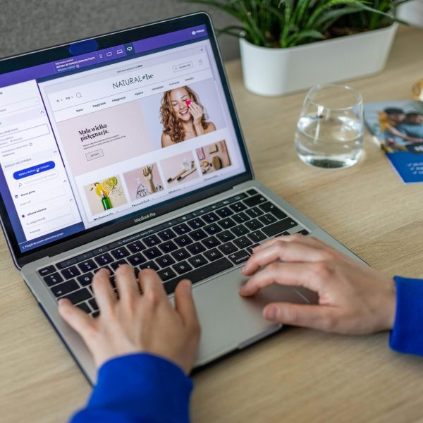 Hands typing on a laptop showing an e-commerce website in a modern office setting.