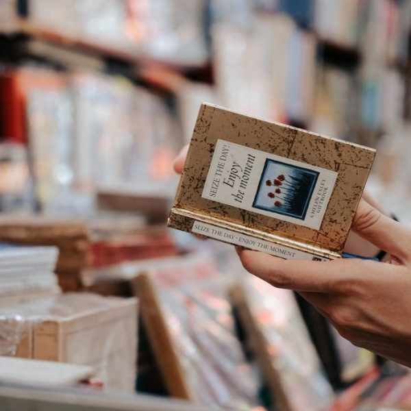 Close-up of a hand holding a book in a cozy, warm bookstore with shelves of books in the background.