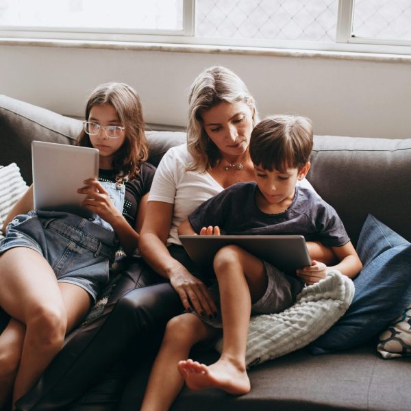 A family enjoying leisure time indoors, using tablets together on a sofa.
