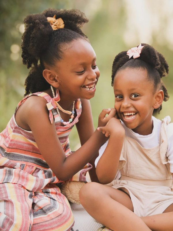 Two young girls sharing a happy moment outdoors, showcasing friendship and innocence.
