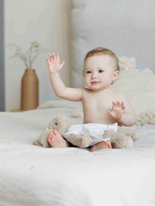 A cute baby happily sitting on a bed with plush toys, radiating a joyful expression.