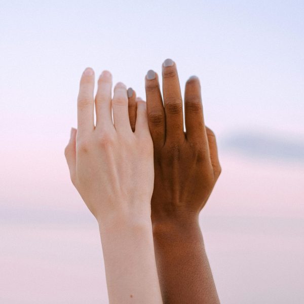 Dos manos de diferentes etnias extendiéndose hacia el cielo, simbolizando unidad y diversidad.