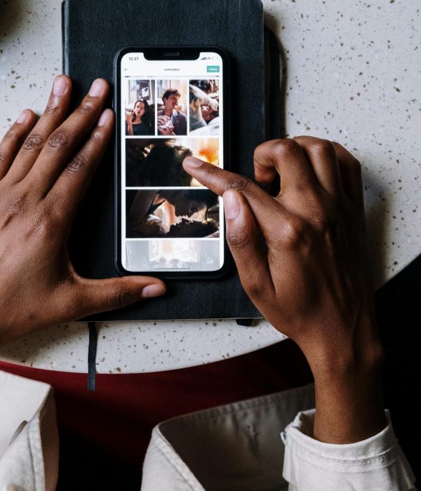 Overhead view of hands using smartphone on top of a notebook, browsing through images on screen.