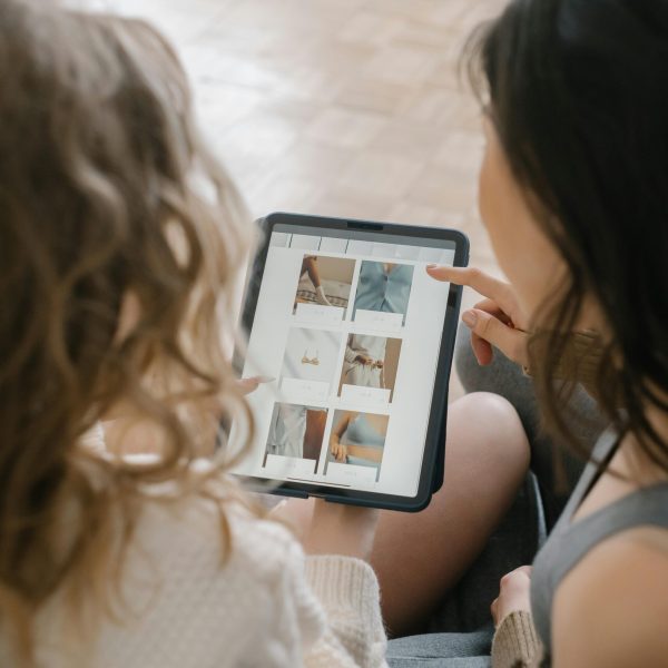 Two women sitting together, shopping online using a tablet, sharing ideas and browsing products.