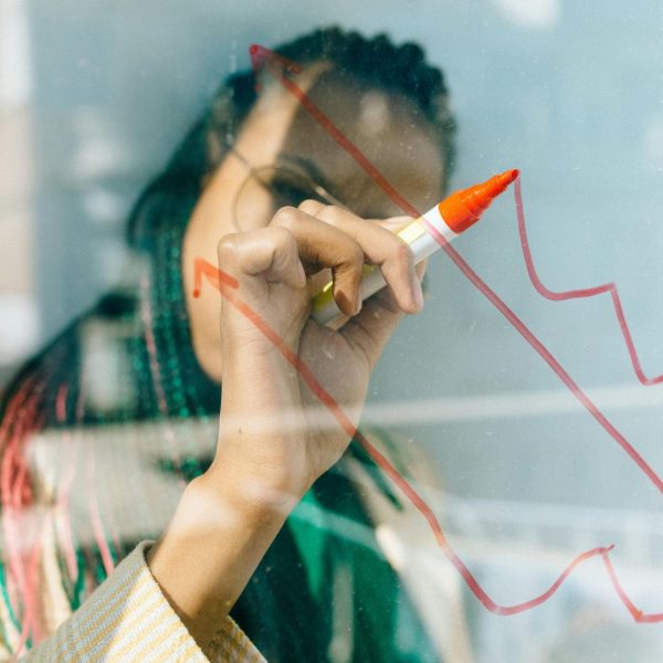 A businesswoman draws a red financial graph on a glass panel, symbolizing strategy and success.