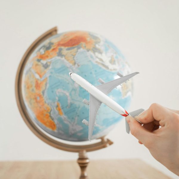Primer plano de una mano con un avión de juguete delante de un globo terráqueo, simbolizando viajes y exploración.