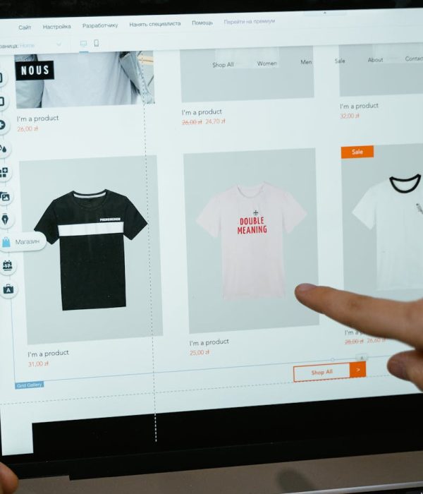 A person points to t-shirt options in an online store on a laptop screen.