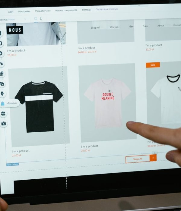 A person points to t-shirt options in an online store on a laptop screen.