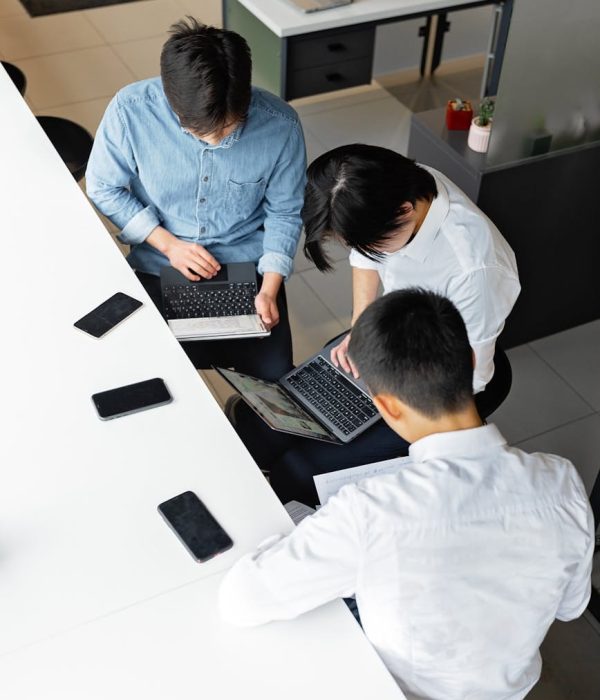 Three colleagues working together at laptops in a modern office setting, viewed from above.